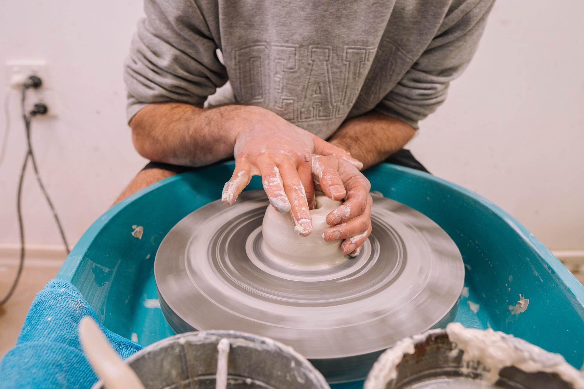 Close up of a person shaping a small vessel on a pottery wheel
